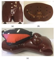 (a) The Alderson Radiation Therapy (ART) female phantom (the arrow indicates TLD placement for measuring the dose to the uterus); (b) slab No. 26 with 16 holes for TLD insertions; and (c) the ART phantom with the water container (10 L) simulating a 60 kg pregnant female.