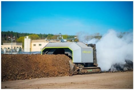 Industrial eWender windrow turner during active compost turning at the Sonnenerde GmbH composting facility. The visible vapour plume illustrates the near-field release of gas and moisture during mechanical agitation.